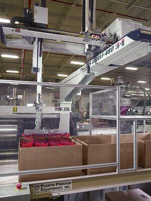 red plastic injection molded parts being stacked into a box in Rodon's facility by an automated arm